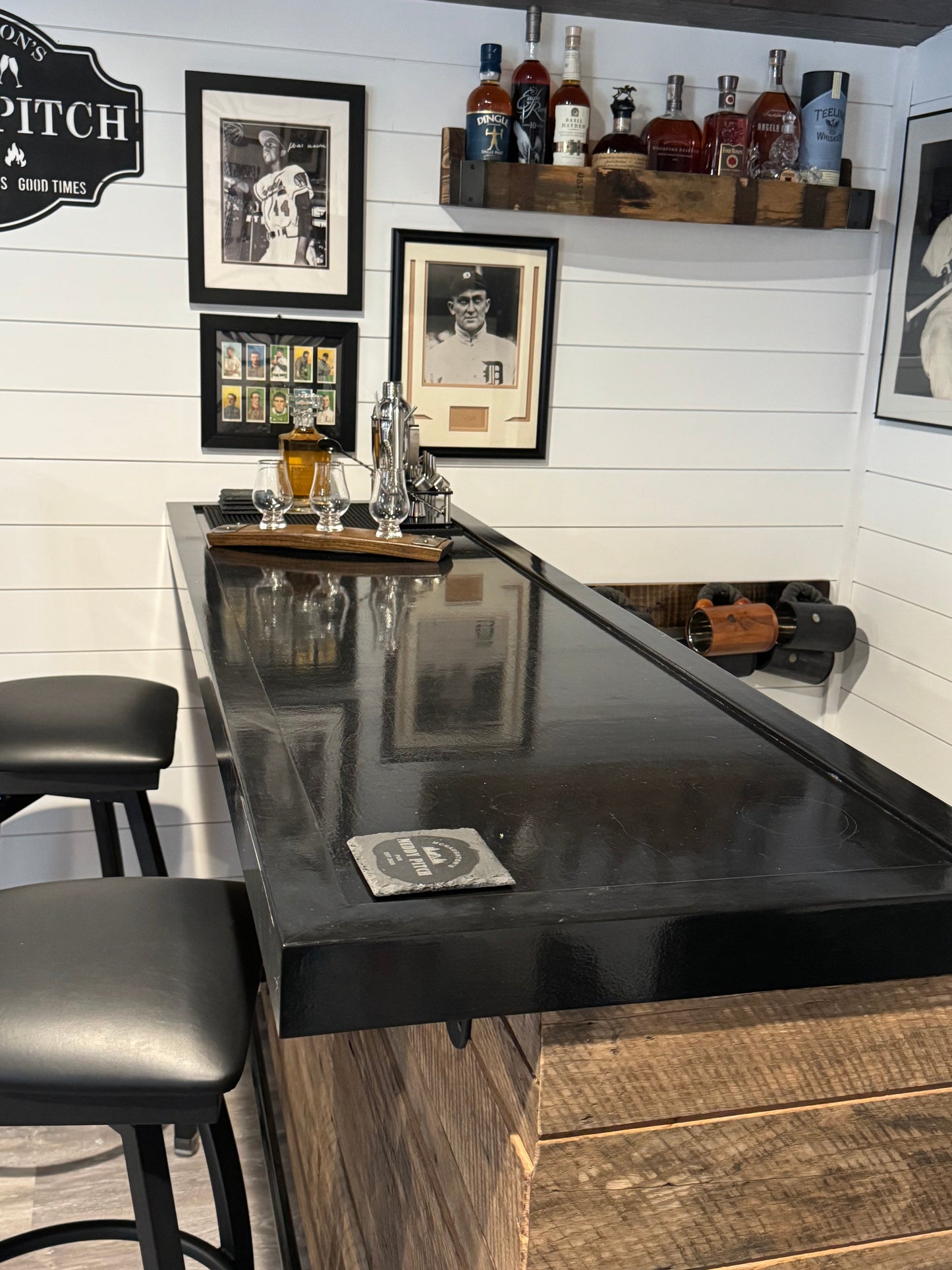 Rustic wood bar with glossy black top and wall-mounted whiskey shelf, built by Red Cloak Wood Designs for home bar setups