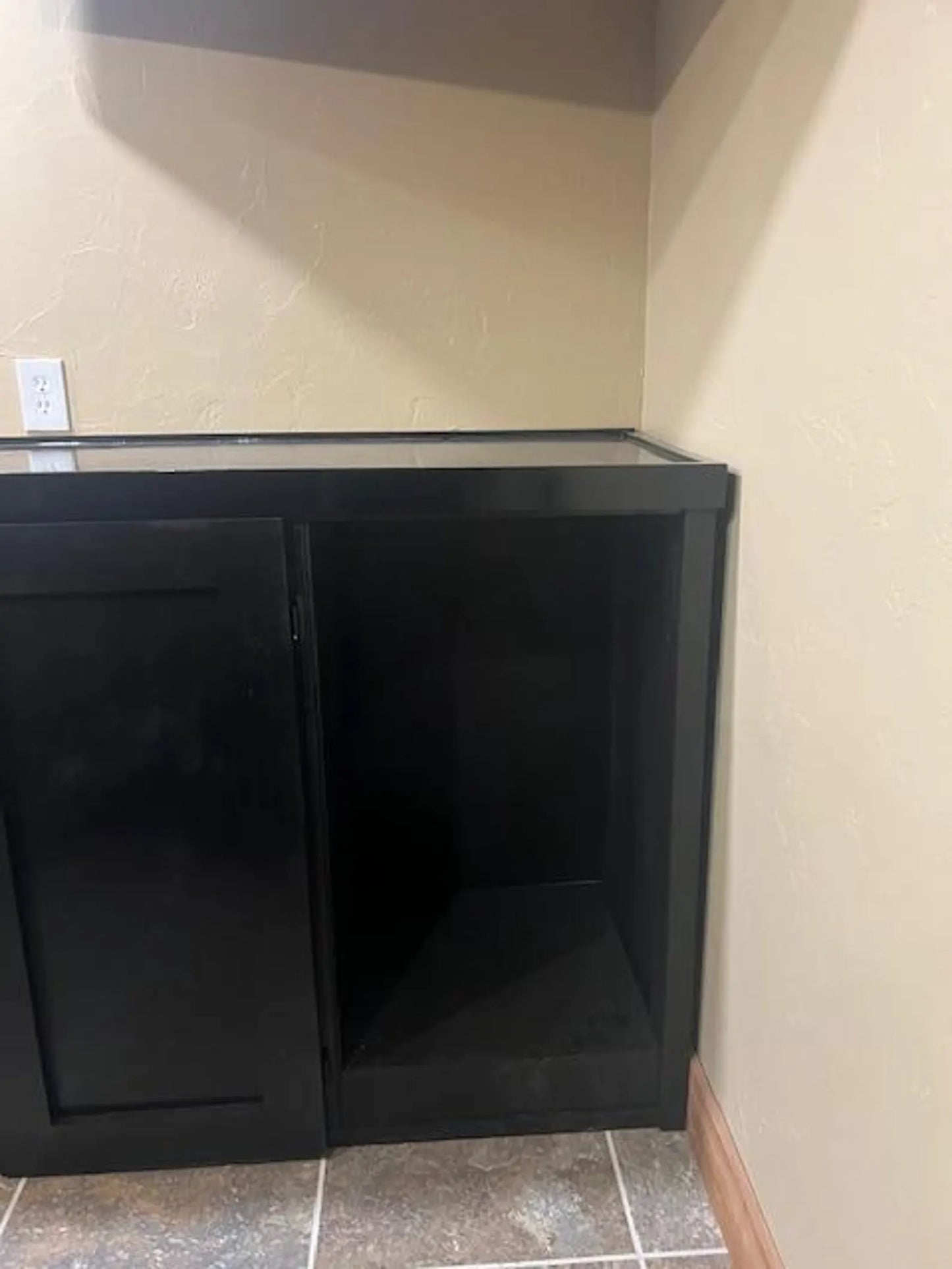 Open black cabinet interior showing bar storage section of U-shaped custom bar, installed in a tiled basement barroom.