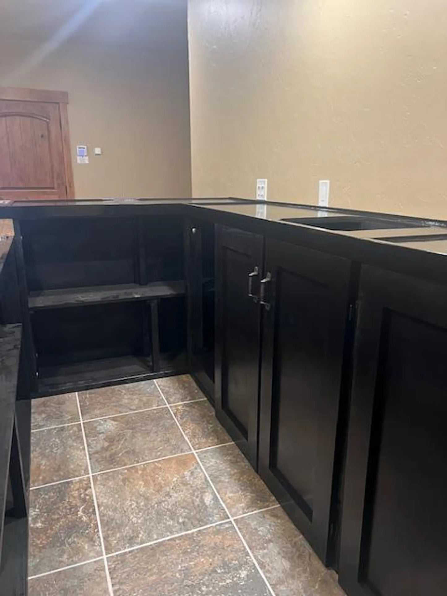 Interior back view of U-shaped wood bar showing black cabinetry, recessed outlets, and tile flooring.
