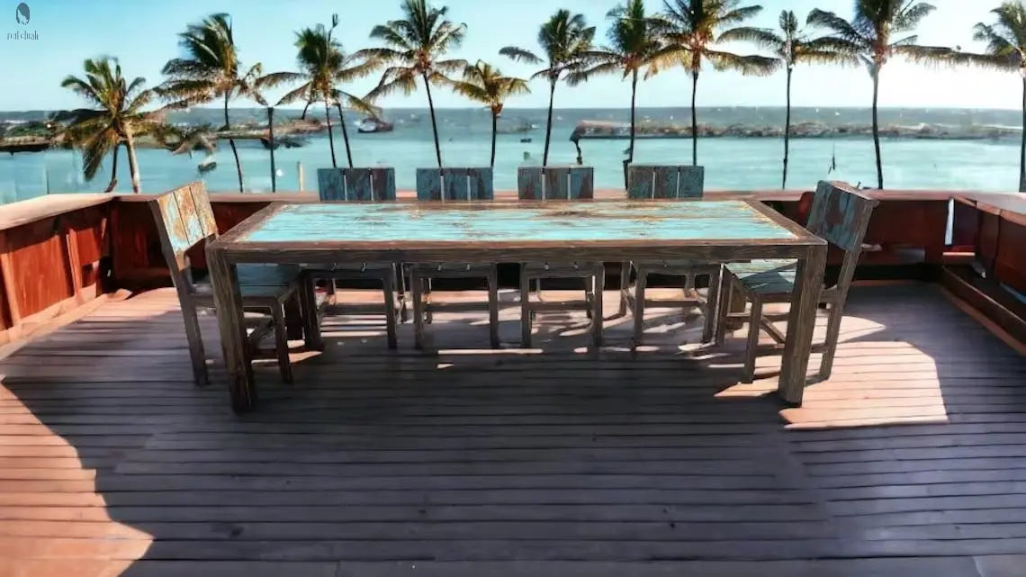Custom outdoor dining table and chairs made from reclaimed barn wood, overlooking the ocean with tropical palm trees in the background