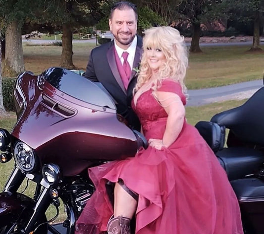 Steve and Debbie Baca of Red Cloak Wood Designs posing on a maroon motorcycle in matching formalwear—celebrating the journey from pandemic pivot to small business success