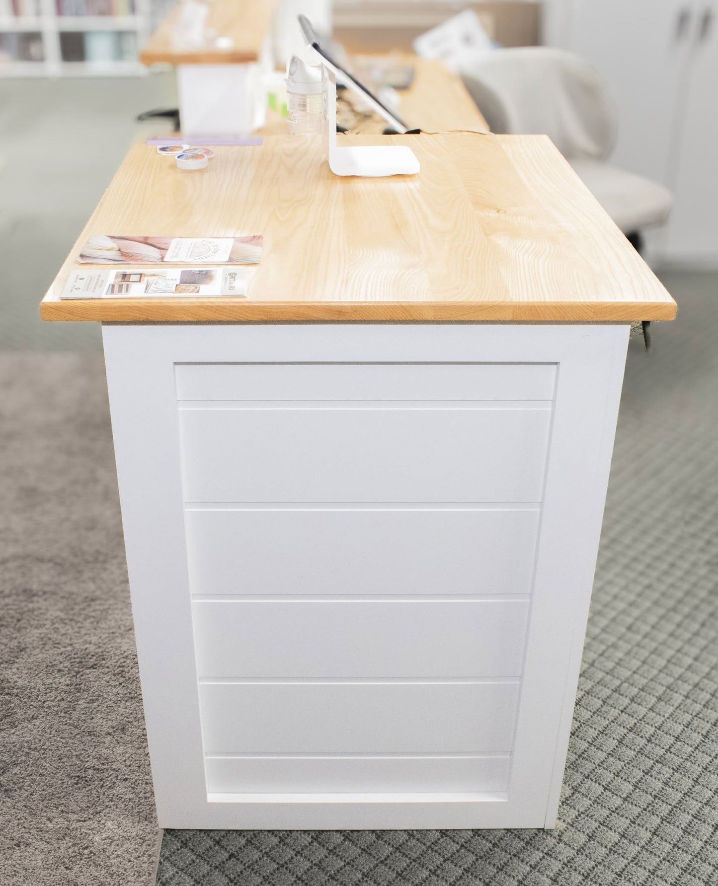 A white reception desk with a light natural wood top, featuring a paneled front and a small tabletop organizer on top.