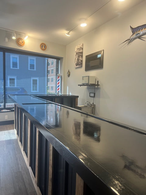 L-shaped commercial counter with glossy sealed black countertop, custom retail checkout counter with wood frame and metal panels in modern service space, USA