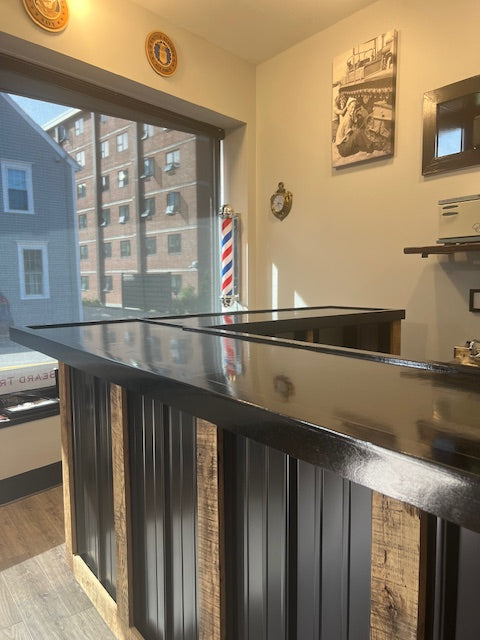 corner angle of L-shaped commercial counter with glossy sealed countertop, custom retail checkout counter with wood frame and black metal panels near storefront window, USA