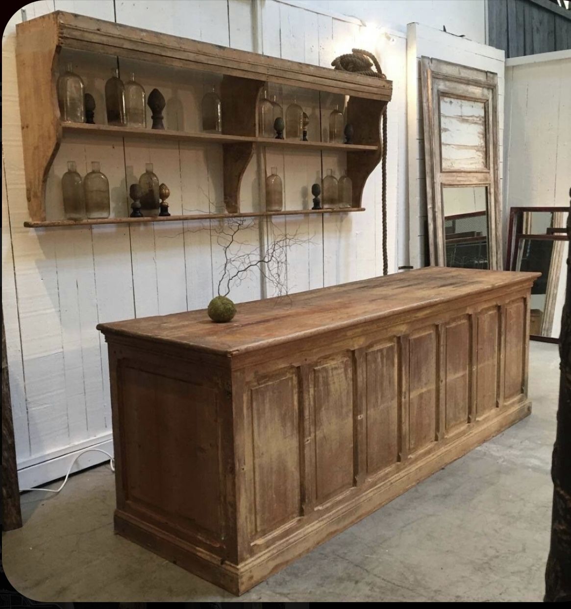 A large rustic custom wooden retail counter / cash wrap / checkout counter / commercial counter with a matching floating shelf unit, shown in a warehouse or showroom setting with white paneled walls and concrete floors.