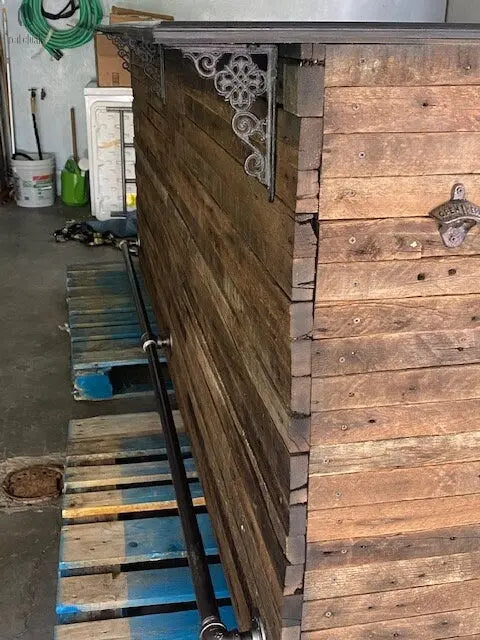 Industrial-style diagonal foot rail with elbow joints and metal flanges on barnwood bar