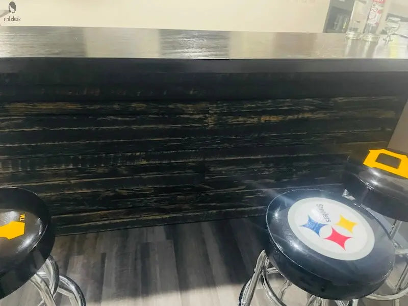 Black-front L shaped wood bar with Pittsburgh Steelers bar stools, reclaimed barnwood front, and solid black bar top by Red Cloak Wood Designs