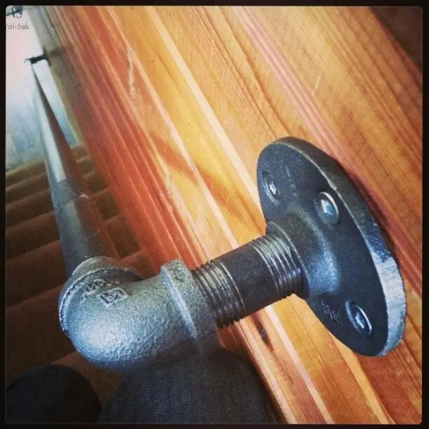 Black galvanized foot rail close-up with flange mount on wood wall at bar angle