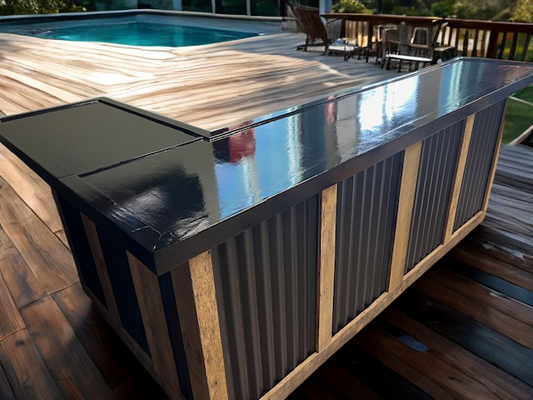 L shaped metal and wood bar by Red Cloak Wood Designs on a wooden deck near a pool, featuring rustic reclaimed wood frame and black corrugated metal panels.