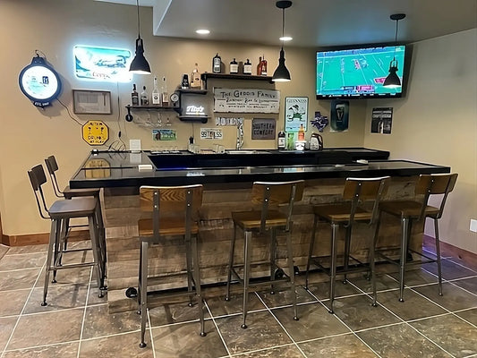 Finished U-shaped home bar setup with 6 metal bar stools, reclaimed wood front, black top, and complete liquor display.