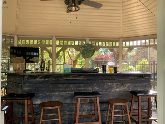 Rustic barnwood tiki bar setup inside gazebo with barstools