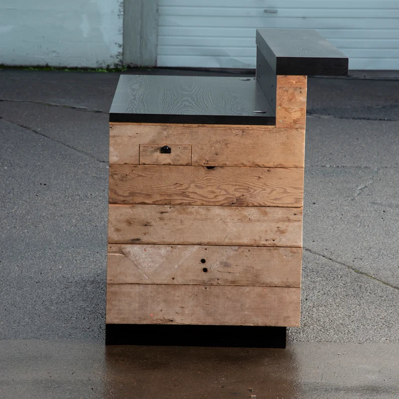 Side profile of a rustic reception desk with reclaimed barn wood panels, black desktop, and transaction counter.