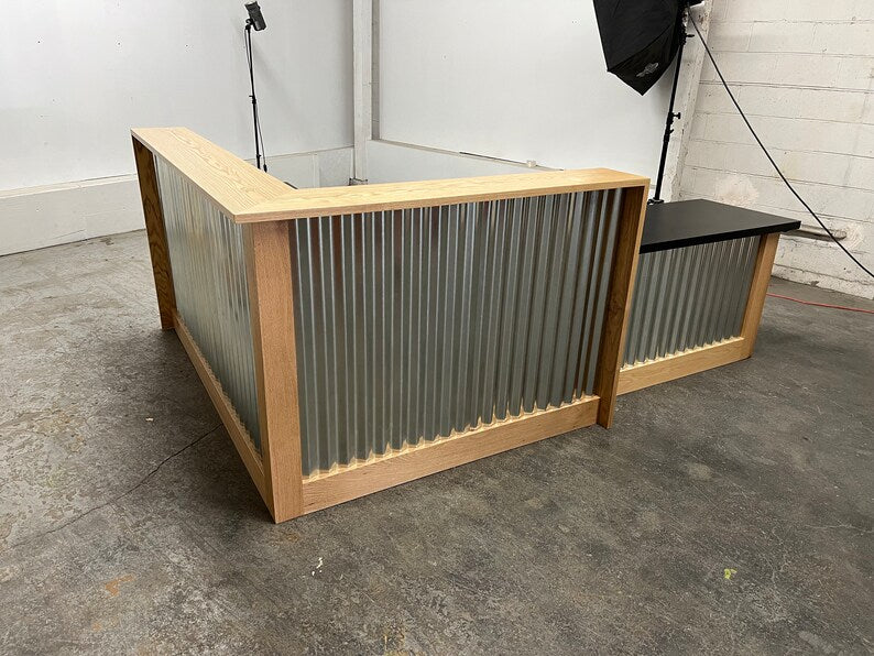 Front and side view of an industrial reception desk with corrugated metal, light wood trim, and black work surface. Handmade by Red Cloak Home