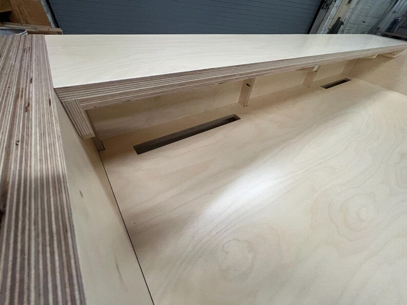 Upper side view of a modern reception desk with layered birch trim and raised transaction counter. Handmade by Red Cloak Home
