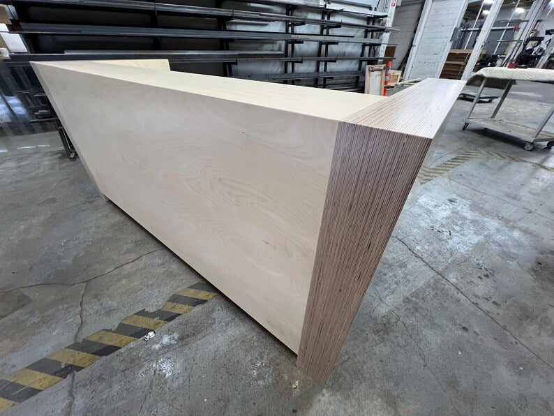 Close side view of a modern reception desk with layered plywood edges and a smooth birch front panel. Handmade by Red Cloak Home