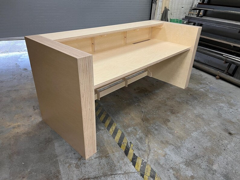 Angled view of a modern birch reception counter with a clean front panel and raised customer ledge. Handmade by Red Cloak Home