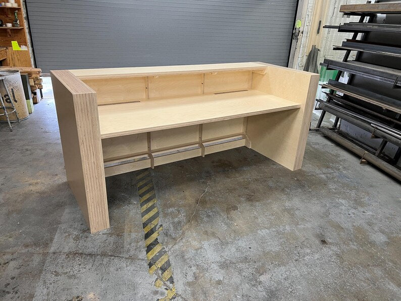 Employee-side view of a birch reception desk with a wide workspace and built-in cord management. Handmade by Red Cloak Home