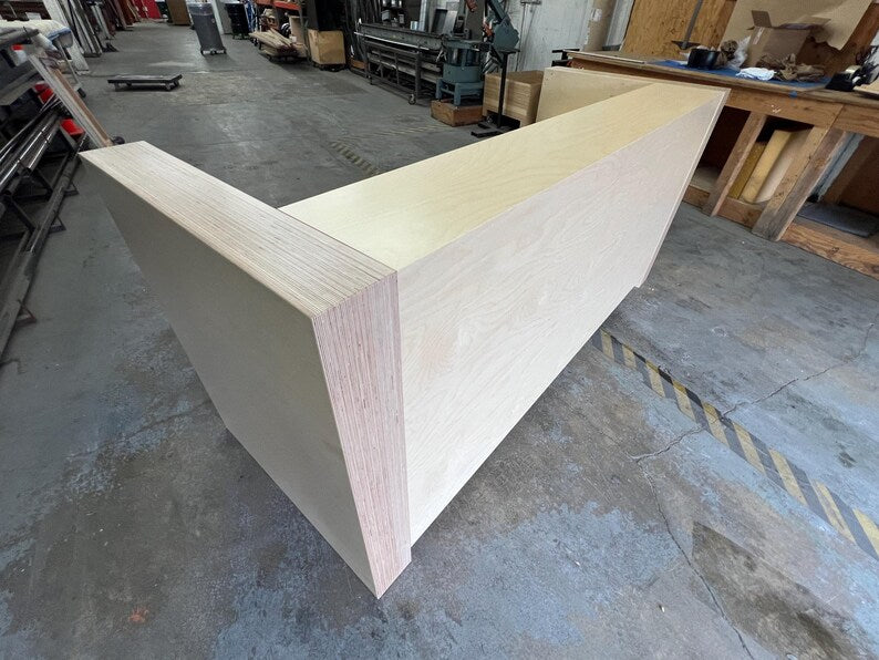 Angled front view of a modern office reception desk with birch panels and thick side trim. Handmade by Red Cloak Home