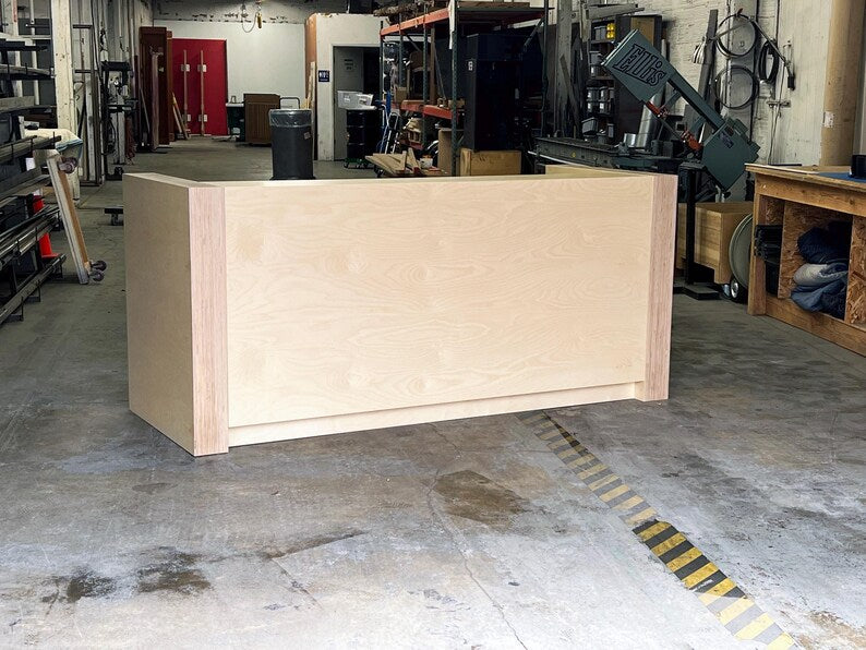 Straight-on view of a custom reception counter with a smooth birch face and raised customer work surface. Handmade by Red Cloak Home