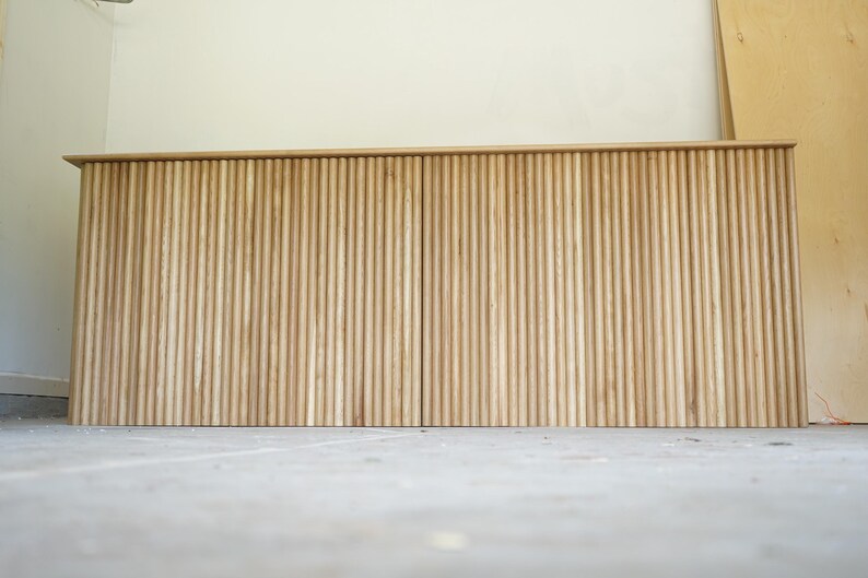 Low front view of a long natural wood checkout counter with vertical fluted panels. Handmade by Red Cloak Home