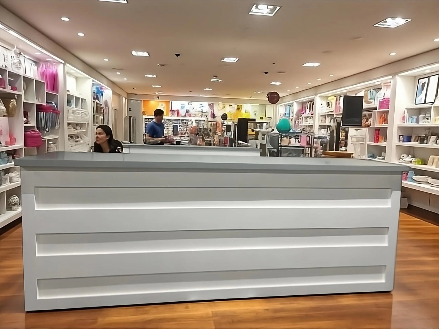 A modern white retail counter / commercial counter with horizontal paneling in a retail store with wooden floors and shelves on both sides.