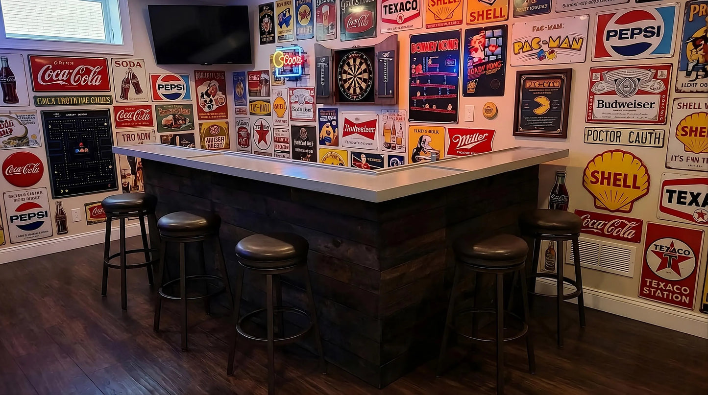 A rustic wood bar with a gray bartop and dark wood base, surrounded by six bar stools in a room decorated with numerous vintage-style Coca-Cola, Pepsi, Texaco, and Shell signs on the walls.
