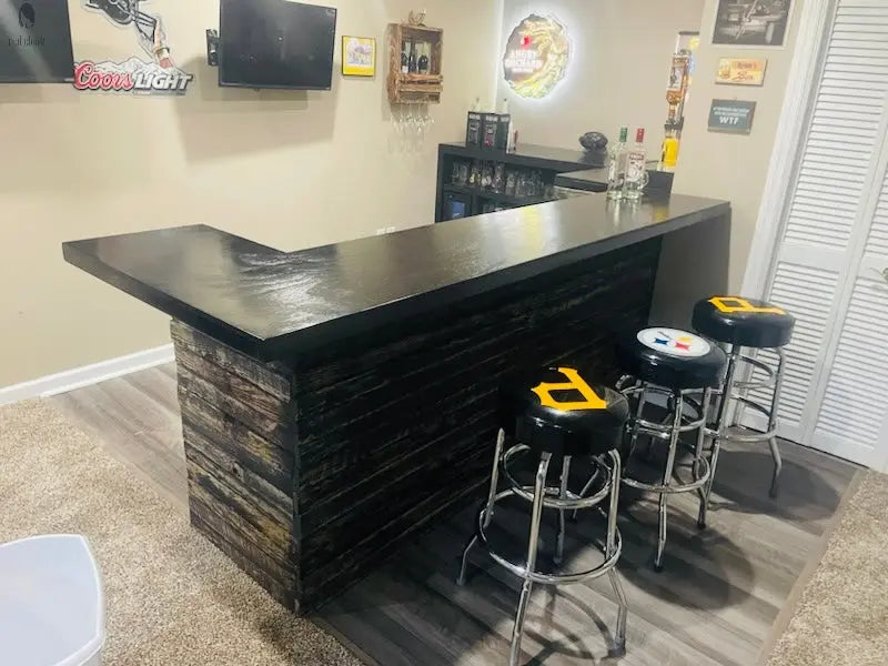 Reclaimed wood L shaped bar with sleek black top and Pittsburgh sports stools, perfect for home entertainment spaces by Red Cloak