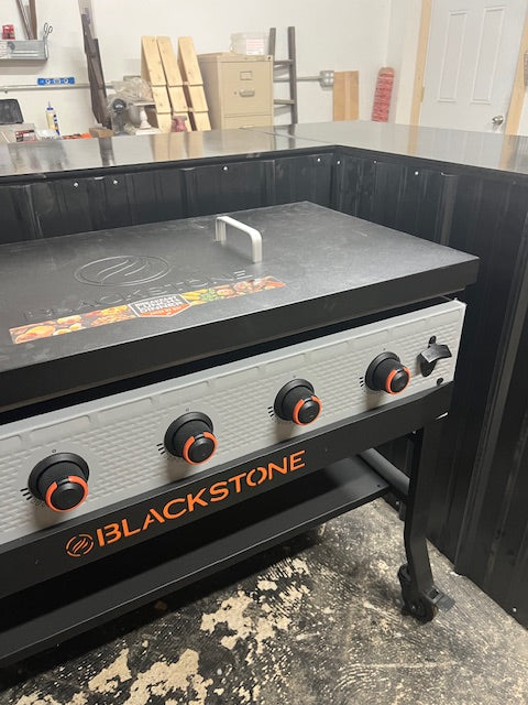 Front close-up of Blackstone Bronco griddle fitted inside Red Cloak Home handmade bar, showing seamless fit, control knobs, and heat-shield interior.