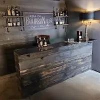 Speakeasy-themed custom wood bar with dark reclaimed finish and bourbon shelf, built by Red Cloak Home