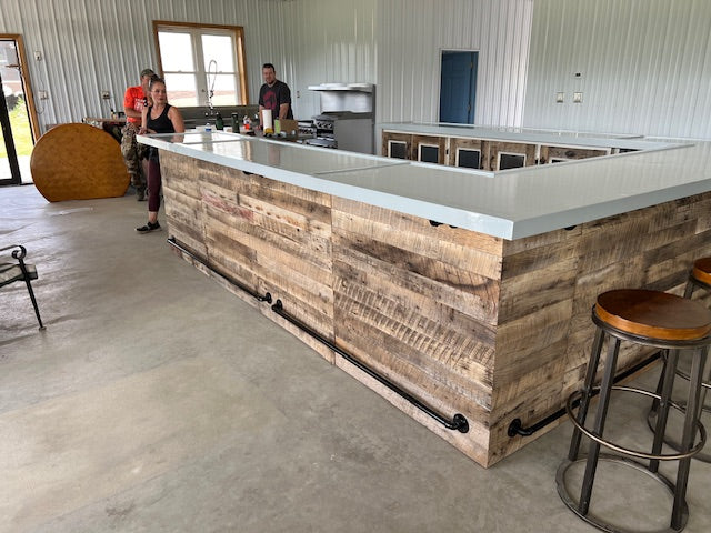 U-shaped wood bar with metal foot rail and white countertop, shown installed in a bright commercial space by Red Cloak Home